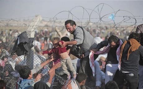 A Syrian refugee hands a baby over the broken border fence into Turkey. AP photo