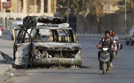 Iraqis ride by a burned vehicle on a Basra street on Saturday. Photo: Haidar Mohammed Ali/AFP
