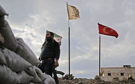 A fighter from Faylaq al-Sham, one of the factions of the Turkish-backed National Liberation Front (NLF) factions, stands in front of the flags of (L to R) the Syrian opposition, the faction, and Turkey, at a position in the village of Kiridiyah, 30 kilometres west of Manbij, January 15, 2019. Photo: Bakr Alkasem / AFP
