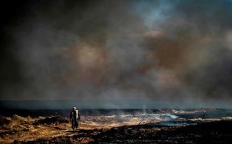 A man walks through a field of billowing smoke in Hasaka province, northeastern Syria on June 10 2019. Photo: AFP / Delil Souleiman