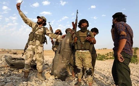 Syrian opposition fighters pose for a picture with the remains of a downed regime warplane near the jihadist-held town of Khan Sheikhun, southern Idlib, August 14, 2019. Photo: Omar Haj Kadour / AFP
