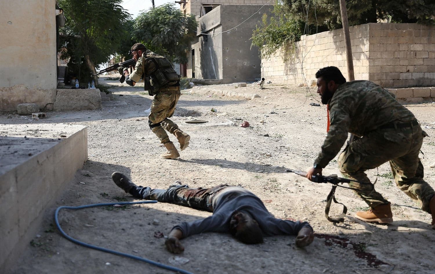 Turkish-backed Syrian fighters take cover next to corpses in the Syrian border town of Ras al-Ain, October 17, 2019. Photo: Nazeer al-Khatib / AFP