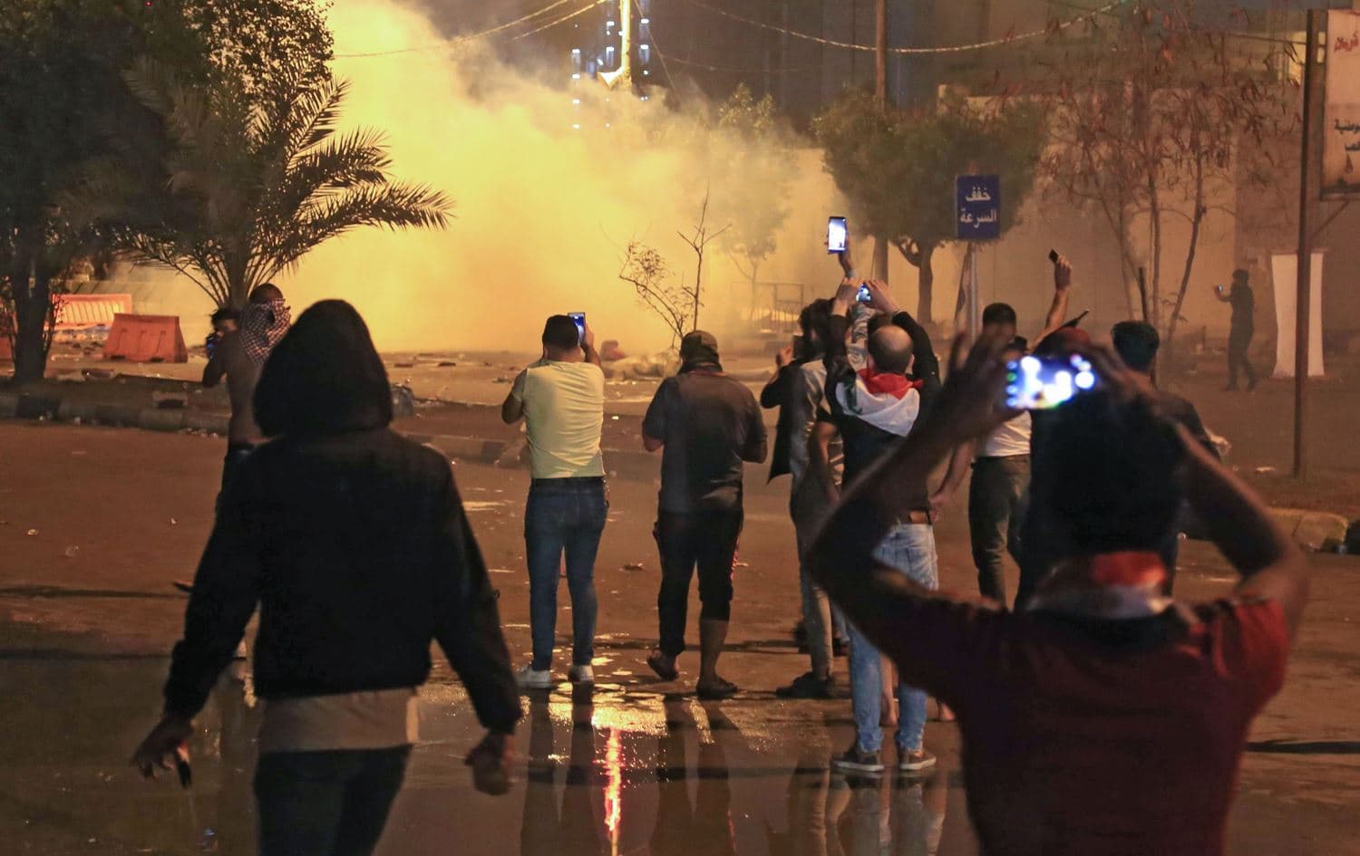 Iraqi protesters film as security forces fire teargas canisters during an anti-government demonstration in the Iraqi Shiite shrine city of Karbala on October 25, 2019. Photo: AFP