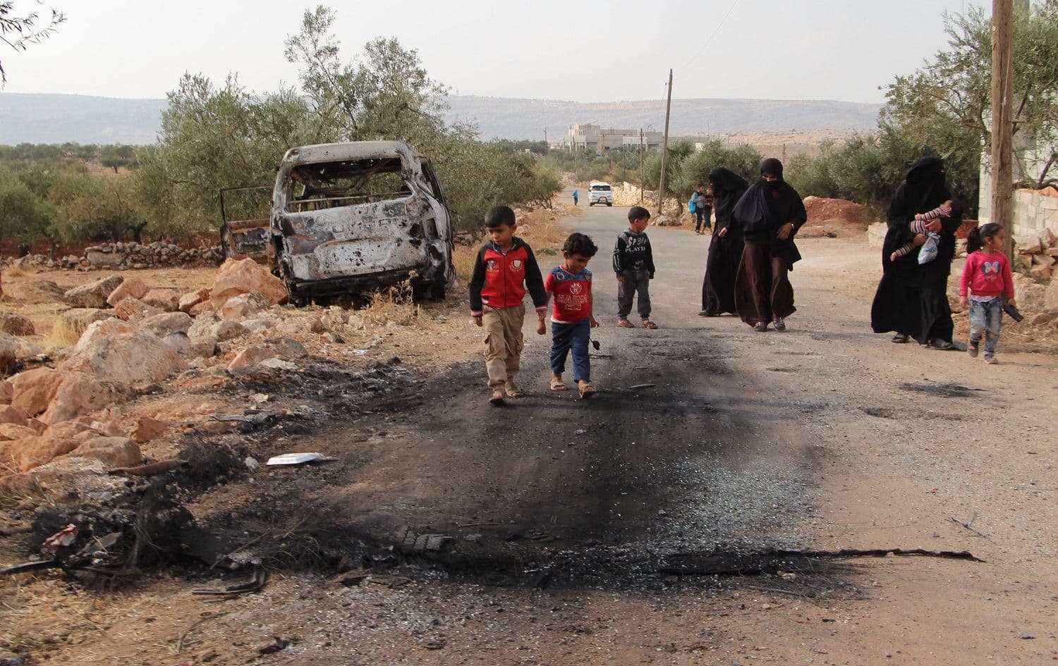 Syrians walk past a damaged van at the site of helicopter gunfire in the village Barisha,where ISIS leader Abu Bakr al-Baghdadi was found on Sunday morning. Photo: Ibrahim Yasouf/AFP