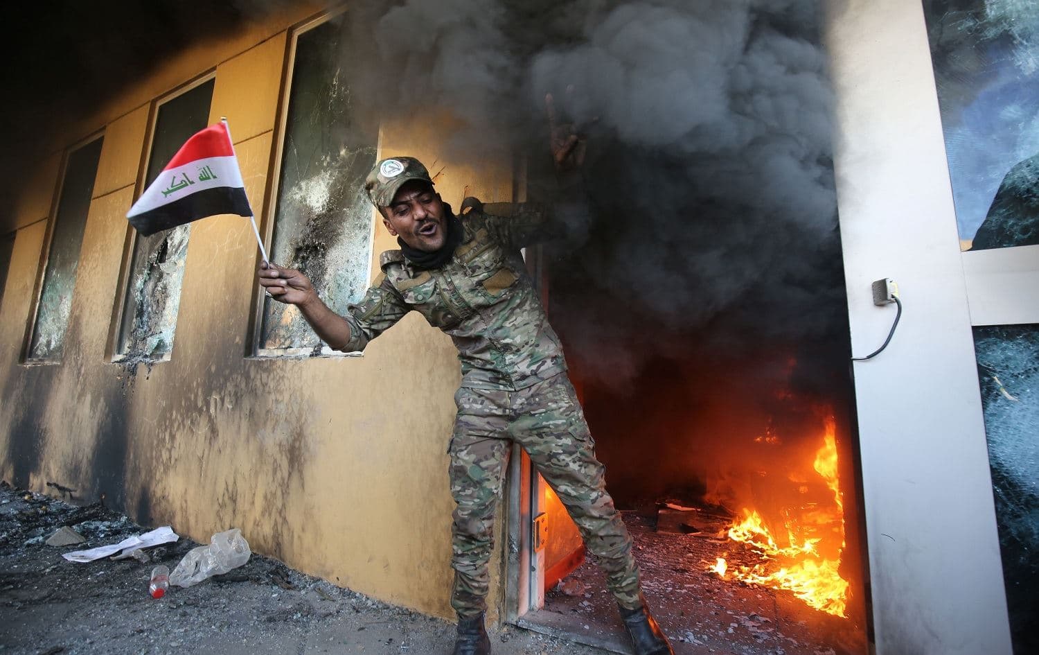 A member of Iraq's Hashd al-Shaabi military network waves a national flag as he exits a burning room at the US Embassy on December 31, 2019. Photo: Ahmed al-Rubaye/AFP