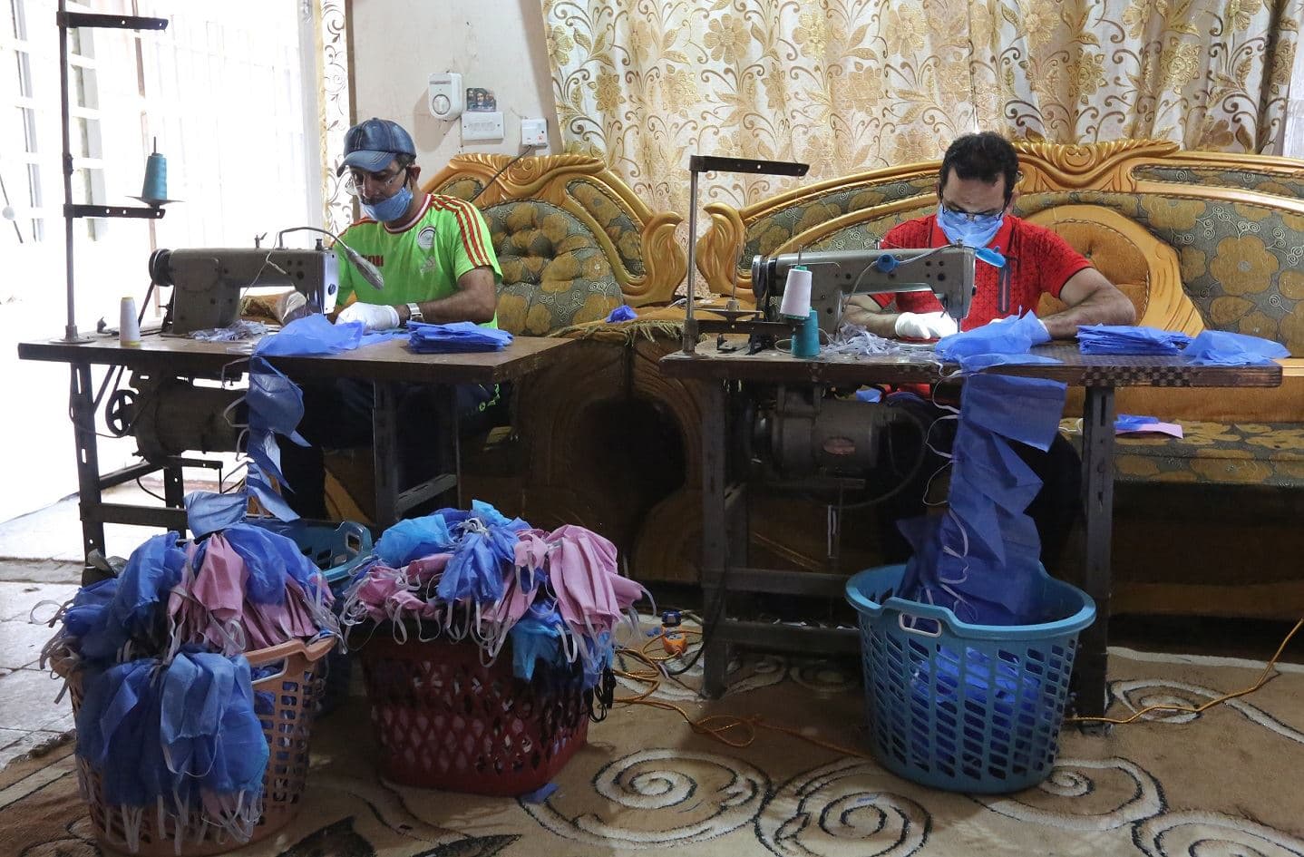 Asaad al-Saadi (L) works at his family's residence in Baghdad with his brother Mohammed after transforming a room in the house into a workshop for manufacturing protective masks and medical decontamination suits on April 3, 2020. Photo: Sabah Arar/ AFP