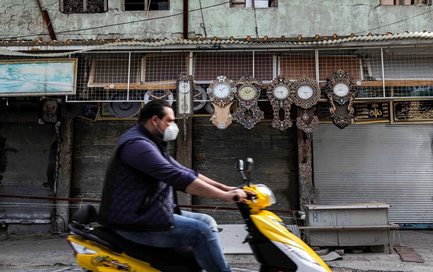 A man wearing a protective mask, as a precaution due to the COVID-19 coronavirus pandemic, drives a scooter past closed shops along a street in Erbil. Photo: Safin Hamed/AFP