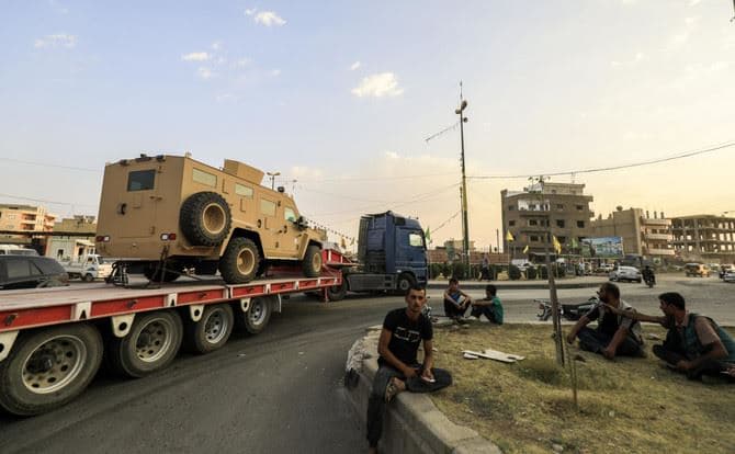Men watch as a military convoy carrying US-made vehicles, bulldozers, and arms headed for Syrian Democratic Forces (SDF) fighting in Raqqa, passes through the northeastern Syrian city of Qamishli. File Photo: AFP