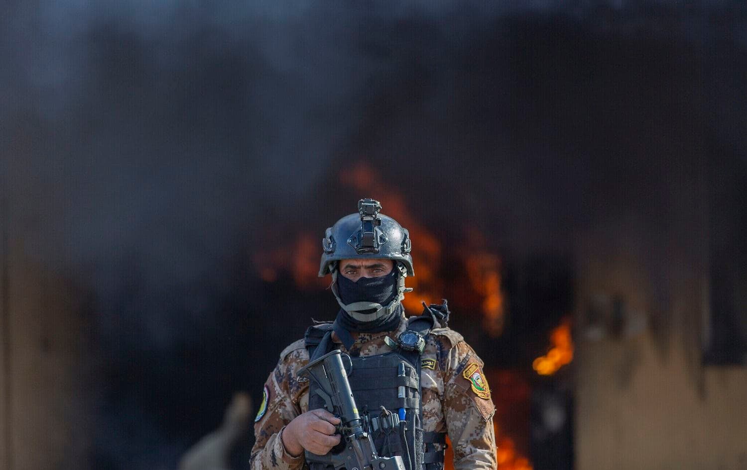 An Iraqi soldier stands guard in front of smoke rising from a fire set by pro-Iranian militiamen and their supporters in the US embassy compound, Baghdad on January 1, 2020. Photo:Nasser Nasser/AP