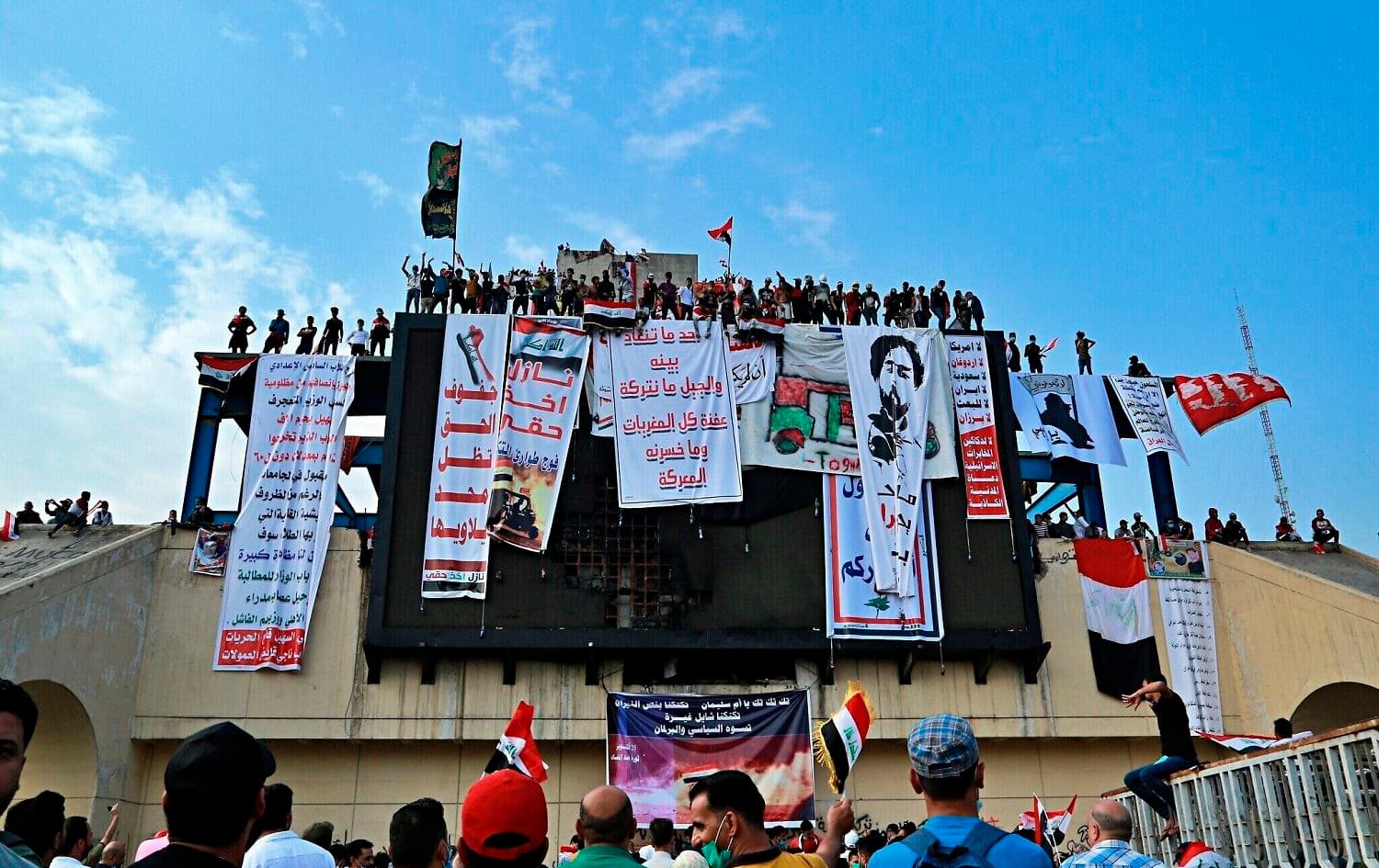 Anti-government protesters hang their demands and slogans while standing on a building near Tahrir Square, Baghdad, Iraq on October 30, 2019. Photo: Hadi Mizban/AP