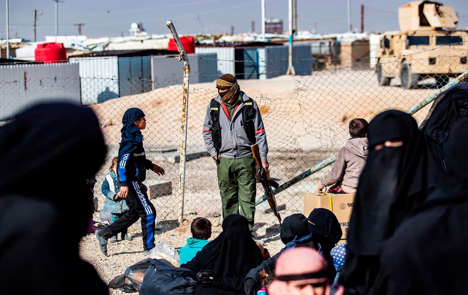 A member of Kurdish internal security stands guard as women lead children ahead of departure during the release of another group of Syrian families from al-Hol camp on January 28, 2021. Photo: Delil Souleiman/AFP