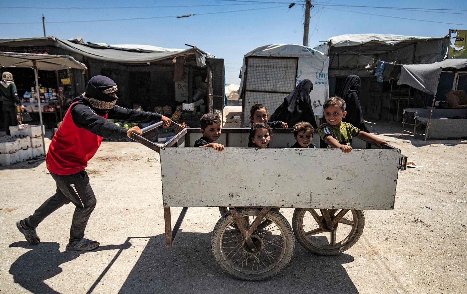 A young man pushes a cart with children inside at al-Hol camp, housing relatives of suspected Islamic State (ISIS) fighters, in Hasaka, northeast Syria on June 23, 2021. Photo: Delil Souleiman/AFP