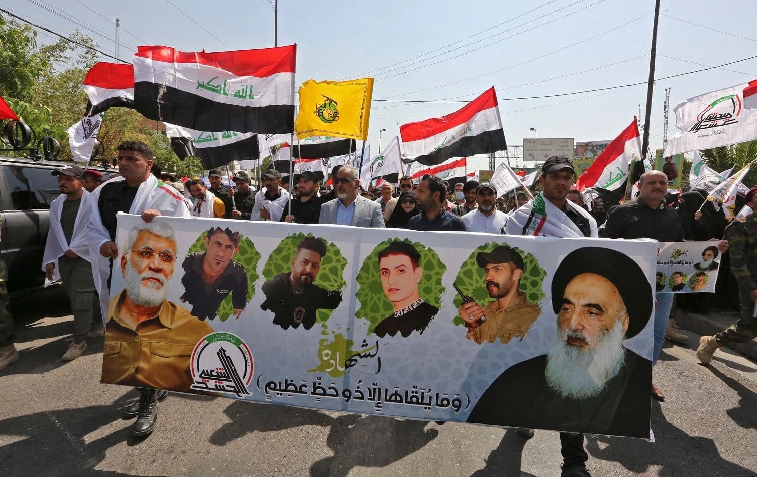 People march with a banner showing (L to R) Iraq's slain PMF commander Abu Mahdi al-Muhandis, other slain members of the group, and Iraq's top Muslim Shiite cleric Grand Ayatollah Ali al-Sistani, during a symbolic funerary parade in Baghdad on June 29, 2021. Photo: Sabah Arar/AFP