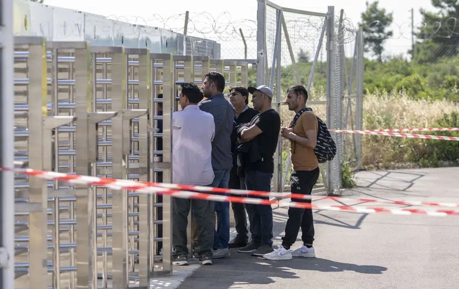A group of men wait at the turnstiles and speak with survivors, mostly from Pakistan, of a deadly migrant boat sinking at a migrant camp in Malakasa north of Athens, on Monday, June 19, 2023. Photo: AP