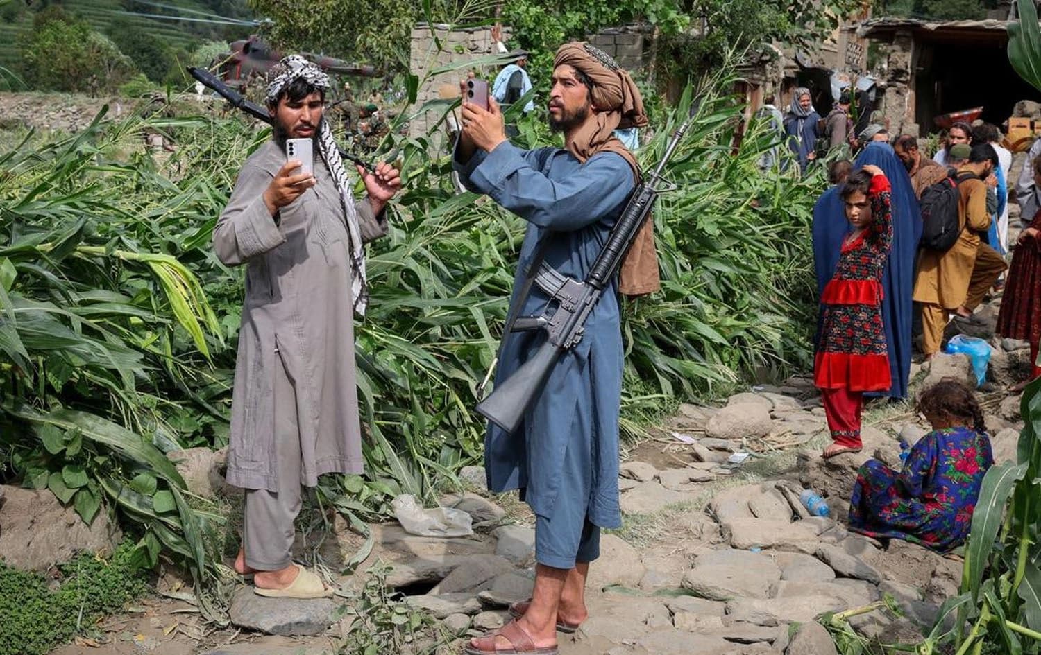 دوو چەکداری تاڵیبان مۆبایلیان بەدەستەوەیە و چەند کەسێک لەوێ دانیشتوون. وێنە: reuters