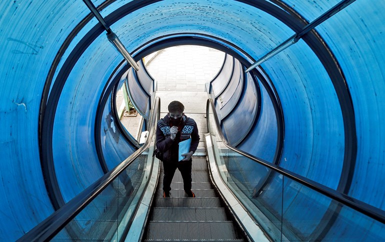 A young man wearing a protective face mask rides the escalator of a pedestrian overpass bridge in Tehran on March 14, 2020. Photo: Stringer / AFP