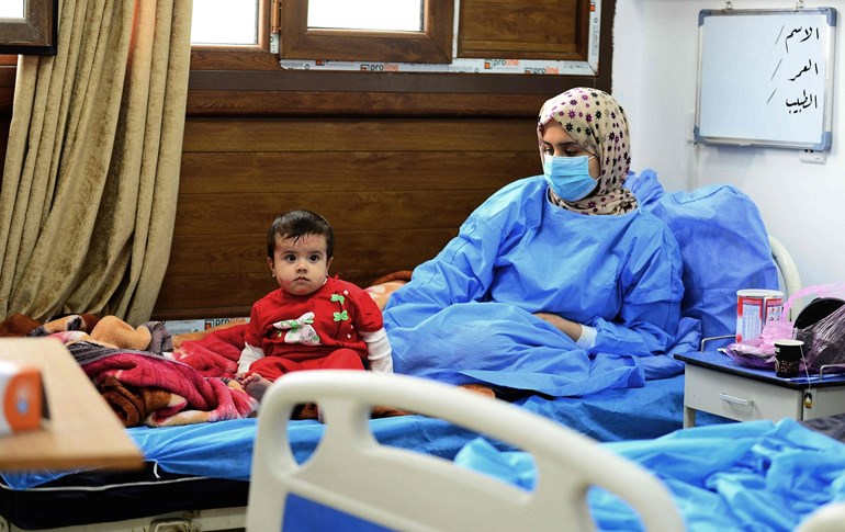 A child sits next to an Iraqi coronavirus patient at a special ward at the Hakim Hospital in Najaf, March 25, 2020. Photo: Haidar Hamdani / AFP