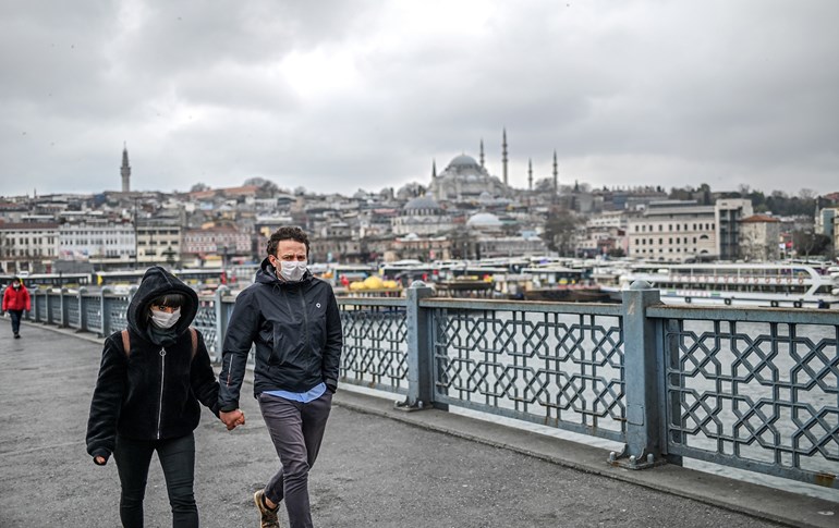 A couple holding hands and wearing facemasks for protective reasons, walk across the empty Galata bridge, on April 1, 2020 in Istanbul. Photo: Ozan Kose/ AFP