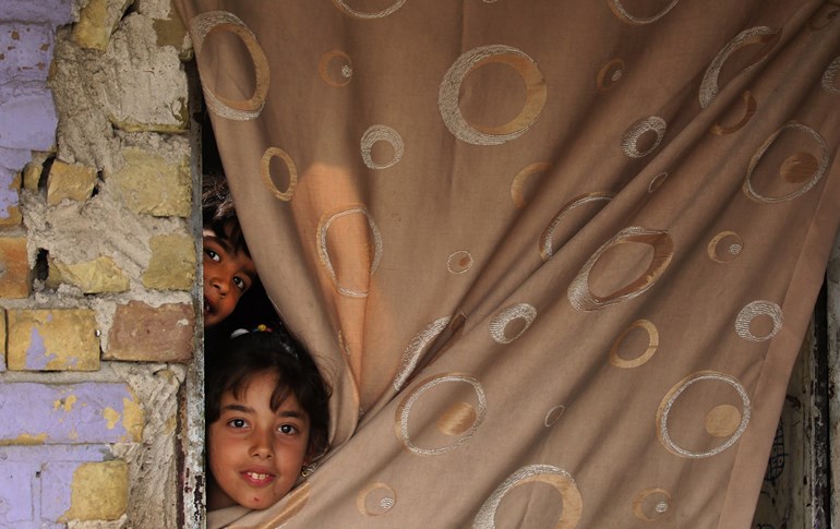 Iraqi children peek out from the entrance of their home in the Washash district, in western Baghdad, on April 6, 2020. Photo: Ahmad Al-Rubaye/ AFP