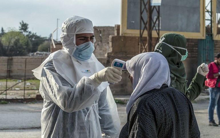 A member of the Kurdish Red Crescent checks the temperature of a passenger upon arrival from Damascus just outside Qamishli on April 7, 2020. Photo: Delil Souleiman / AFP