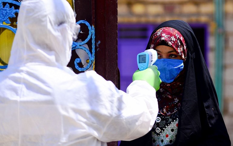 An Iraqi medic takes the temperature of a woman in Iraq's central shrine city of Najaf, April 20, 2020. Photo: AFP