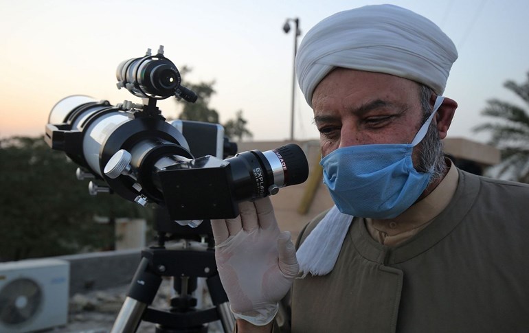 A Sunni Muslim cleric wearing a face mask uses a telescope to gaze while searching for the crescent moon marking the beginning of Ramadan in Baghdad on April 22, 2020. Photo: Ahmad al-Rubaye / AFP