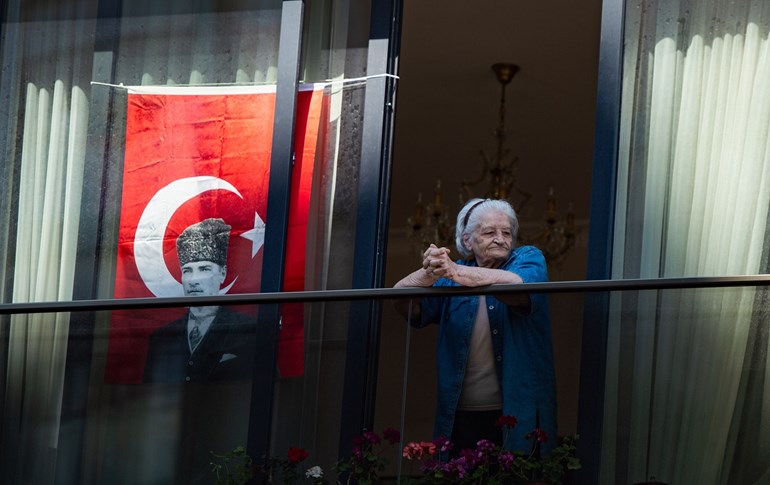 An elderly woman stands on her balcony next to a Turkish flag bearing a picture of Mustapha Kemal as she attends festivities marking the National Sovereignty and Children's Day, On April 23, 2020 in Istanbul. Photo: Yasin Akgul/AFP