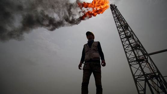 کارمەندێکی کۆمپانیای نەوتیی لە عێراق کە گڕی ئاگری نەوتەکە لە پشتییەوە دەبینرێت، وێنە: AFP