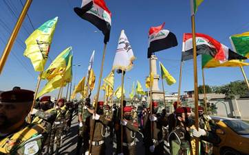 Fighters lift flags of Iraq and paramilitary groups during a funeral in Baghdad following a US strike. Photo: Ahmad Al-Rubay/AFP