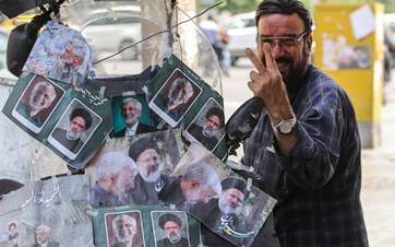 An Iranian motorcyclist gestures as he stands near his bike plastered with pictures of Iranian presidential candidate Saeed Jalili and Iranian late president Ebrahim Raisi, in Tehran on July 4, 2024. Photo: RAHEB HOMAVANDI / AFP